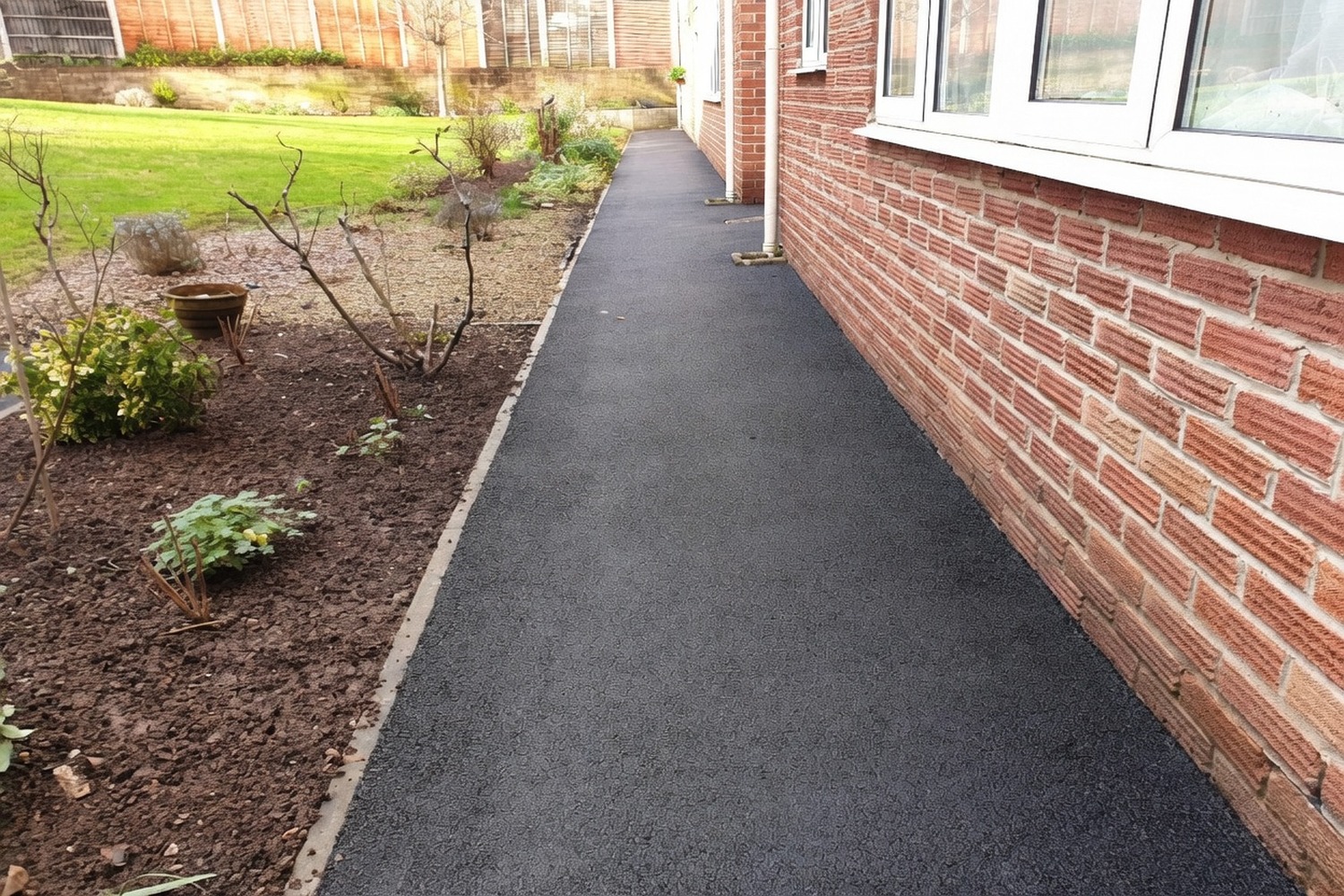 Fresh tarmac path running along a brick building, finished tight to the wall