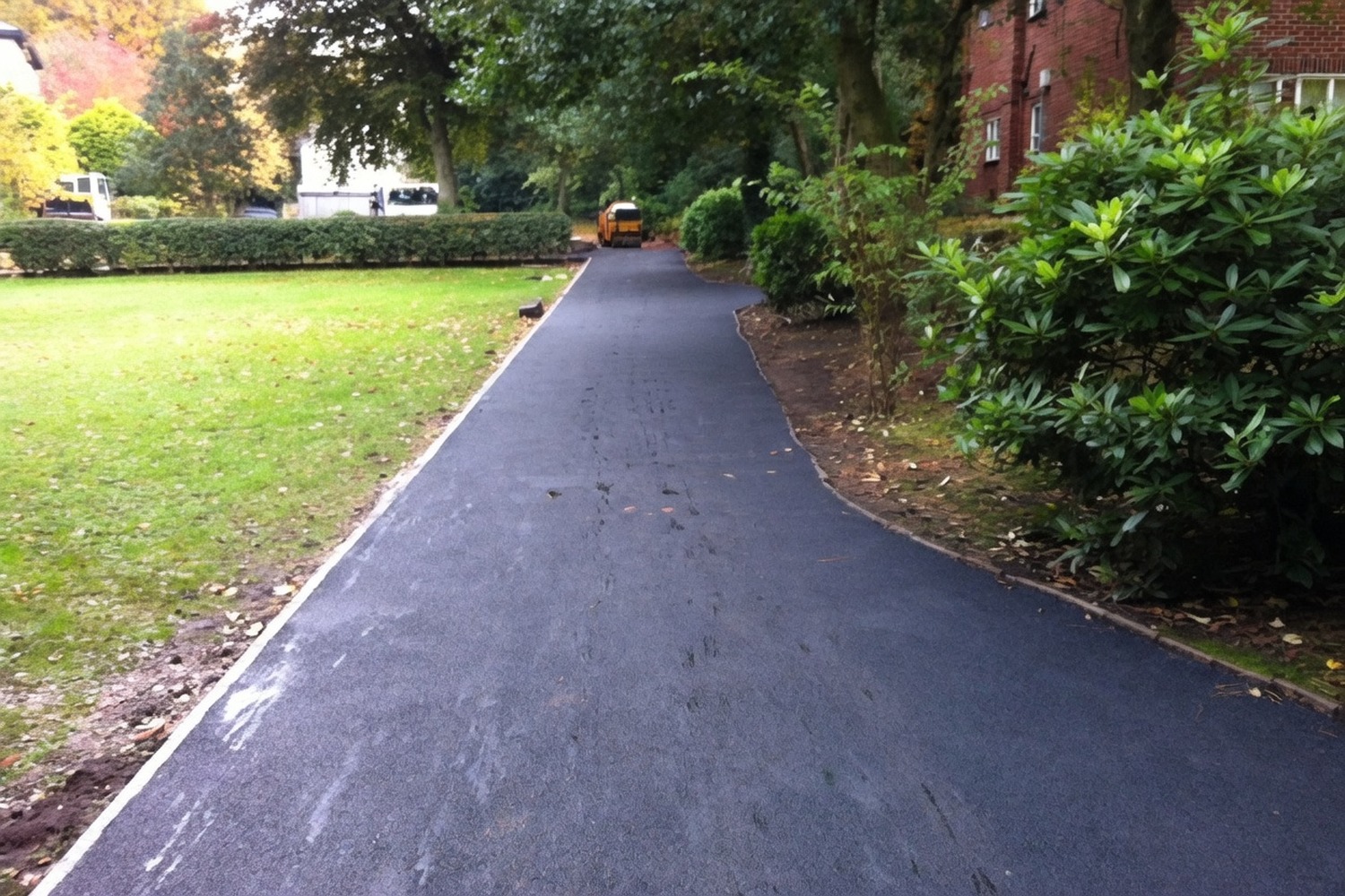 Long fresh asphalt path running through a parkside garden