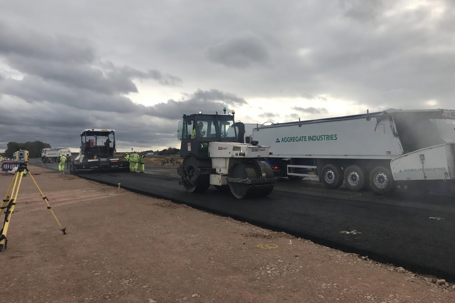 Paver and roller working in sequence on a fresh asphalt section