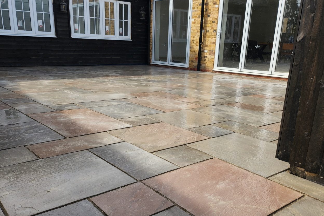 Finished sandstone patio behind a black-clad rear extension with bifold doors, wet after final wash