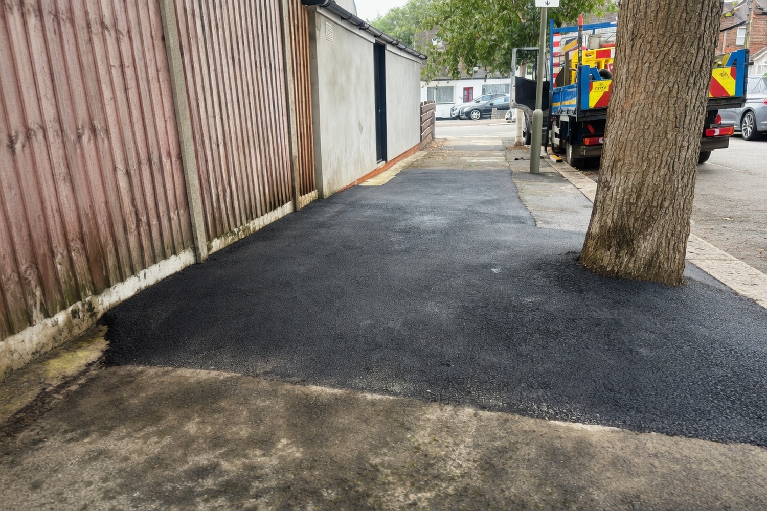 Asphalt path repair beside a timber fence with works truck